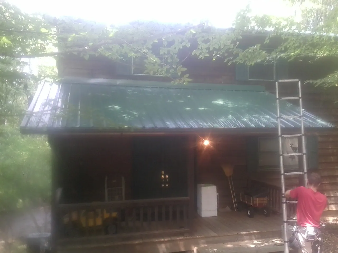 Worker on a ladder at the green porch roof of a wooded cabin in Freeport